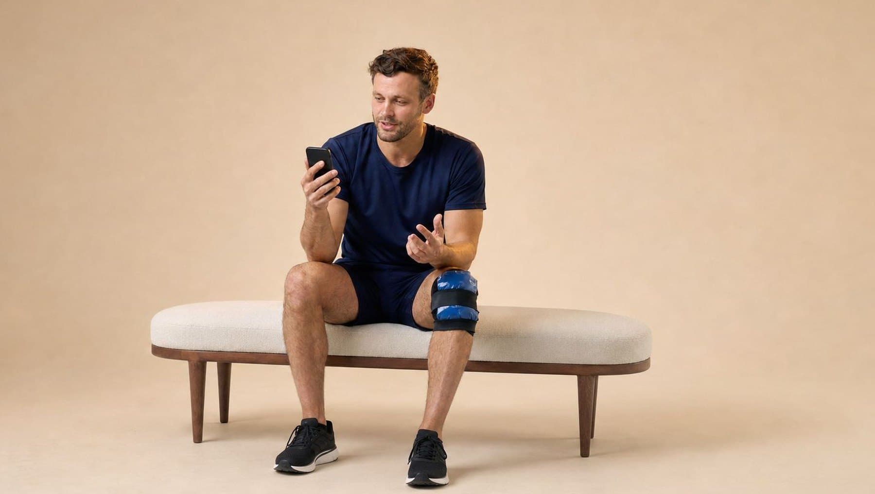A man in navy training gear with ice strapped to his knee, on a video consult on his phone