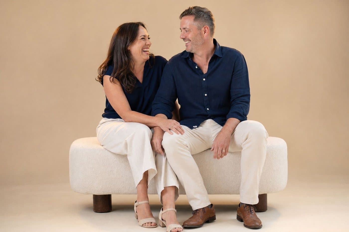 A couple laughing together on a cream bench