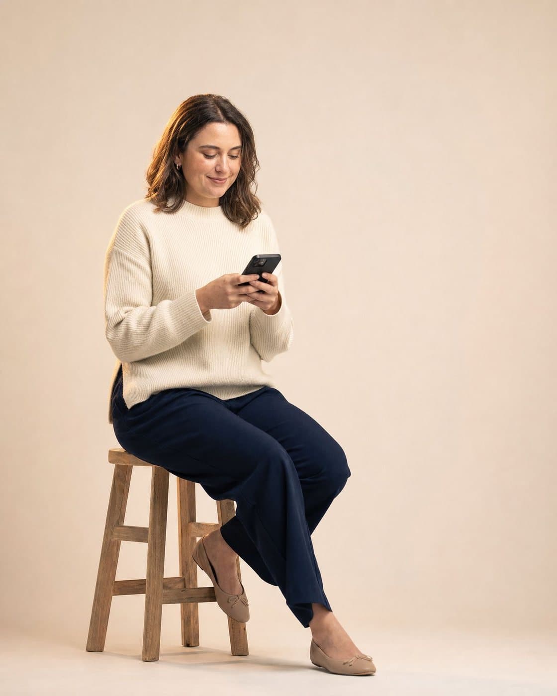 A woman sits on a stool looking at her phone.