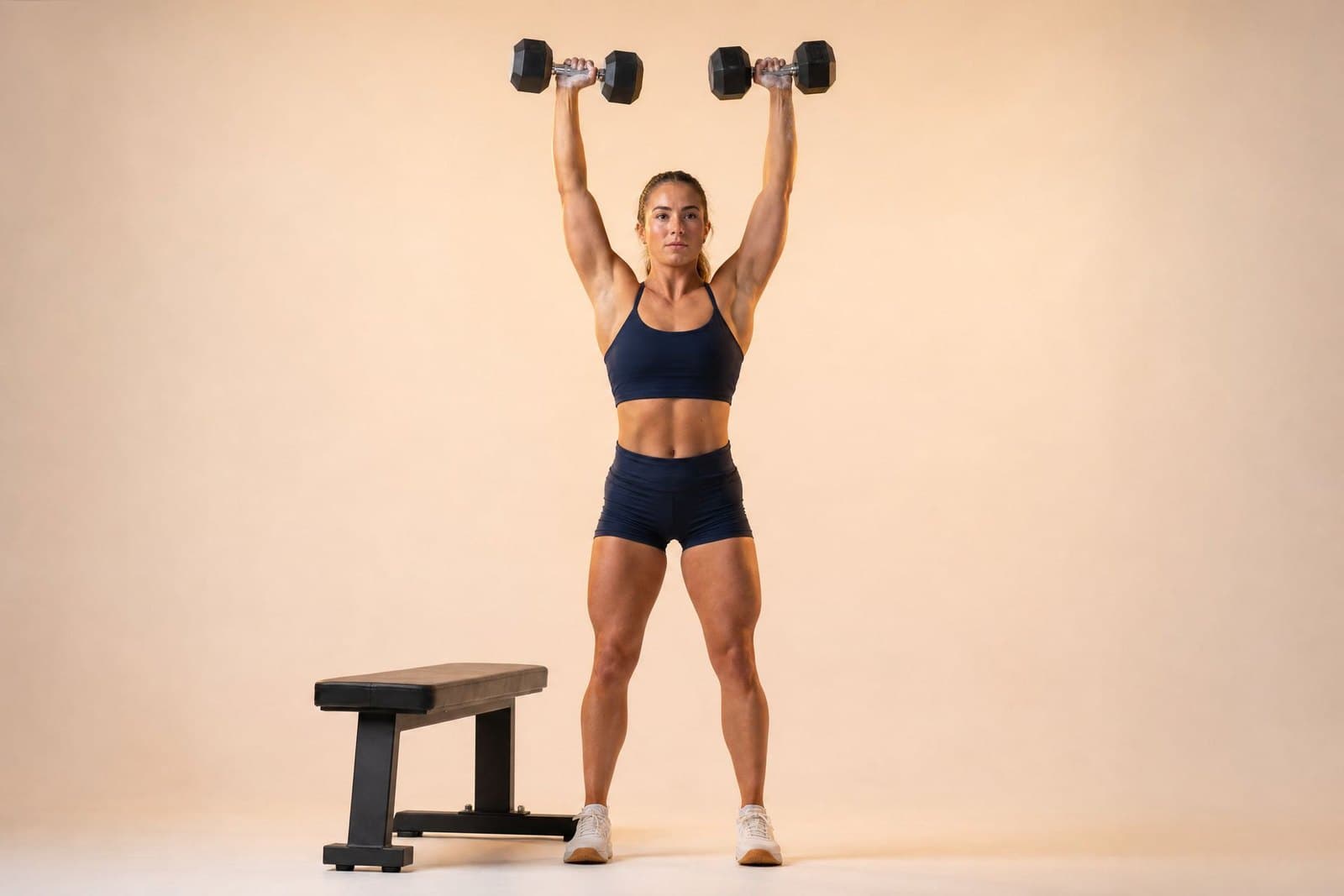 A natural female physique athlete pressing dumbbells overhead