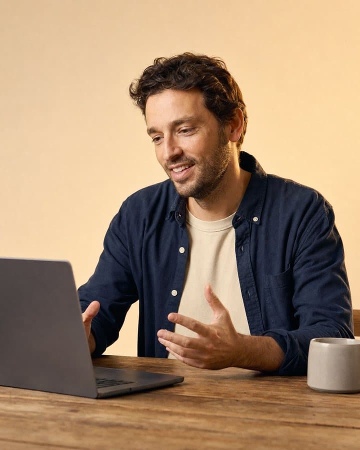 A man on a video consult at a timber desk, leaning in