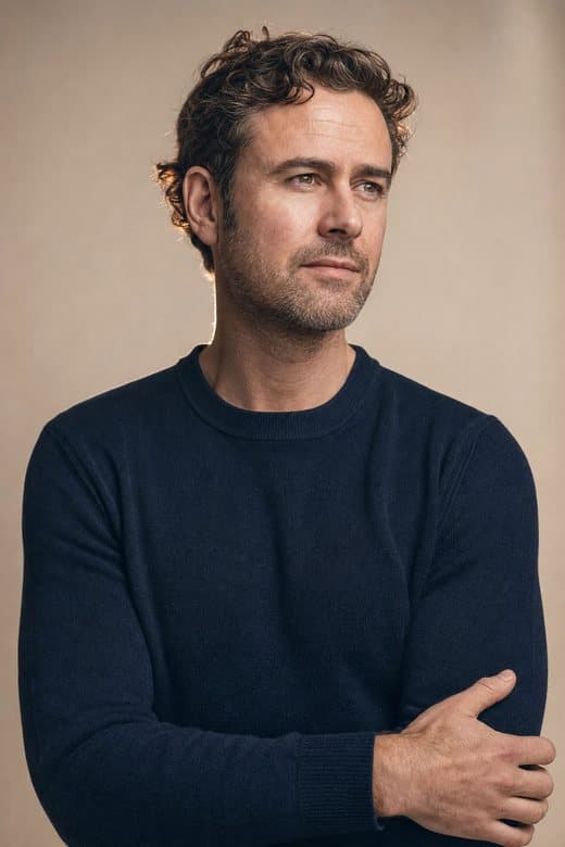 A man in a navy jumper, arms folded, quietly confident