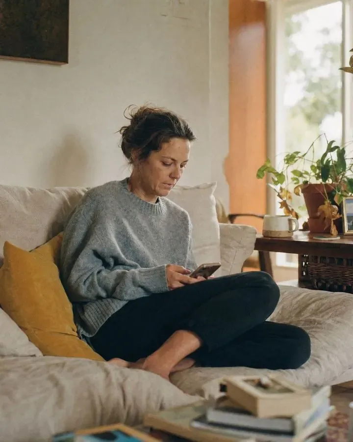 A woman looks at her phone while sitting on a sofa.