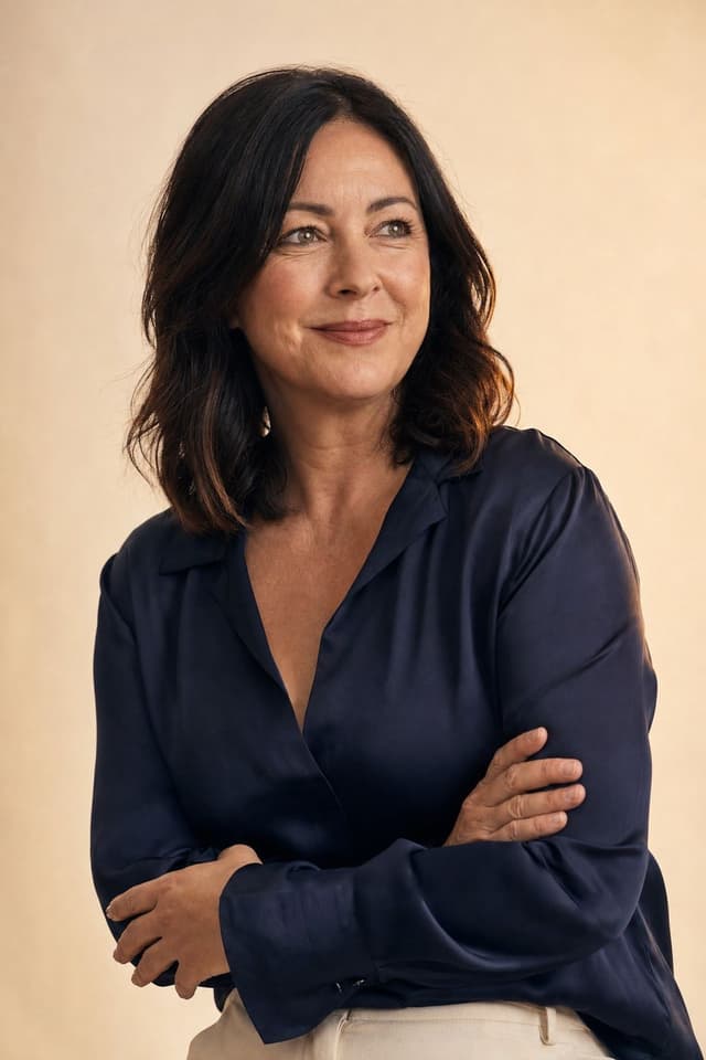A woman in a navy blouse, arms folded, thoughtful