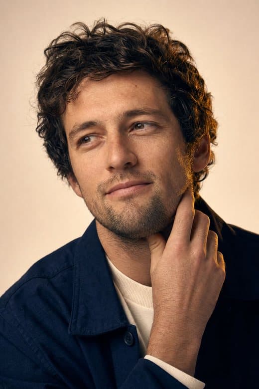 A man in his late thirties, hand at his jaw, calm and thoughtful
